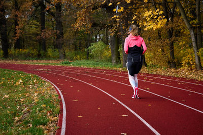 Woman running at track. female runner jogging at stadium. active sport exercises at autumn day