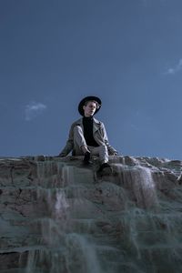 Woman sitting on rock against sky