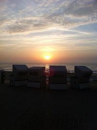 Hooded chairs on beach against sky during sunset