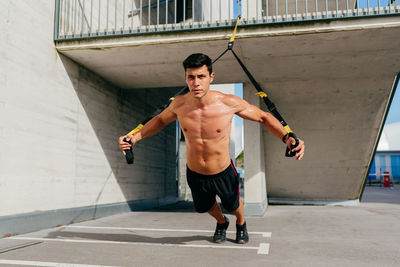 Determined male athlete with muscular body training on street with trx ropes and looking away