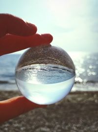 Close-up of hand holding crystal ball on beach