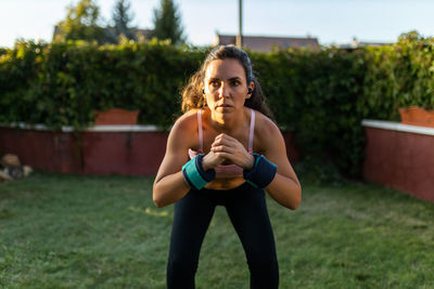 Fit female athlete in sportswear using laptop and doing squats while following online tutorial during training in backyard at sunset