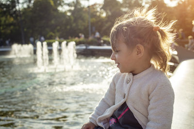 Adorable toddler girl looks at the fountains in the park in the park on a sunny day