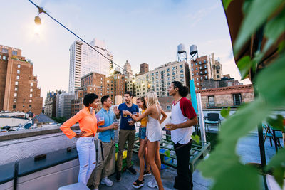 Friends with drinks standing on building terrace in city