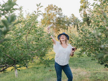 Young caucasian millennial girl at apple orchard enjoying red wine and apples 