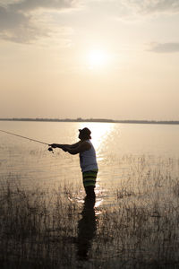 Rear view of silhouette man standing by sea against sky during sunset