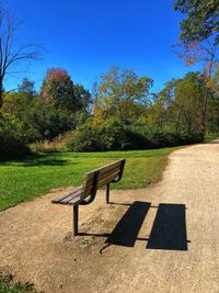 Empty bench in park against clear blue sky