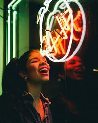 Young woman laughing against neon sign on window during night