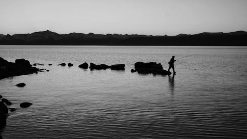 Silhouette ducks swimming in lake against clear sky