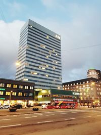 Traffic on road by buildings against sky in city