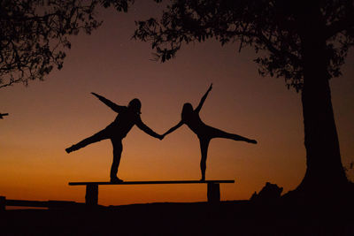 Silhouette people with arms raised against orange sky