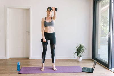 Young pretty girl working out at home with dumbbells