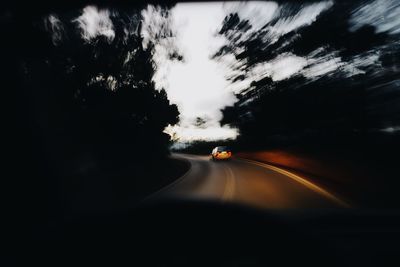 Road amidst silhouette trees against sky seen through car windshield