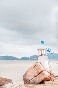 Lifeguard hut and rocks at beach against cloudy sky