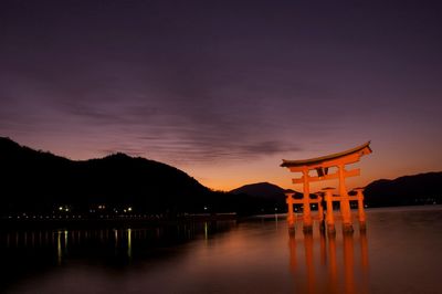 Itsukushima shrine at lake against sky during sunset