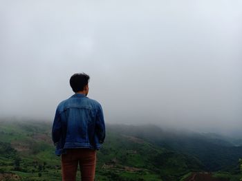 Rear view of man standing on mountain against sky