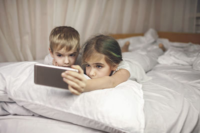 Siblings watching video in mobile devices in bed, gadget dependence and addiction, online lifestyle