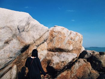 Rear view of woman standing by rock against blue sky