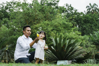 Man holding daughter playing with bubbles in park