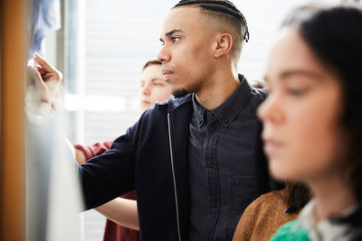 Young man checking test results on bulletin board while standing with friends at university