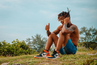 Full length of young man sitting on field against sky