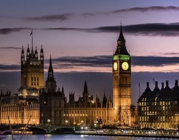 Clock tower amidst river and buildings against sky at dusk