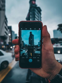 Cropped image of hand holding smart phone in city