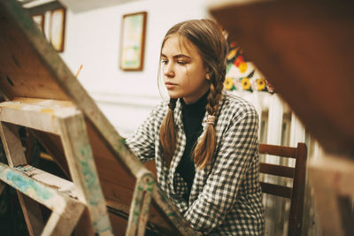 Art school, creativity and people concept - woman with easel, palette and brush painting at studio