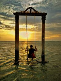 Silhouette boy on beach against sky during sunset