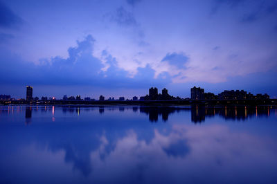 Silhouette buildings reflecting on calm lake against sky during sunset