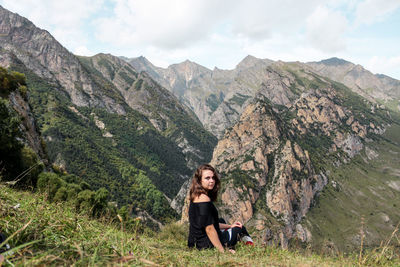 Portrait of young woman sitting against mountain range