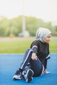 Thoughtful female athlete stretching at stadium