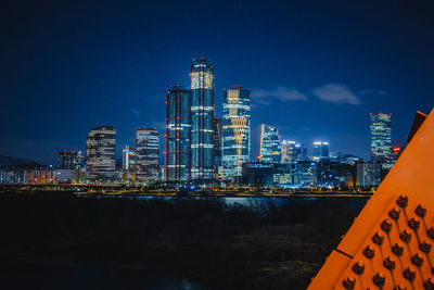 Illuminated buildings in city against blue sky