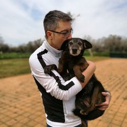 Man holding dog while standing on footpath