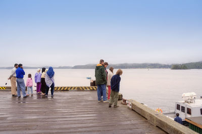 People standing on pier over lake against clear sky