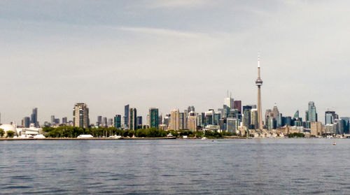 Distant view of cn tower in city by lake ontario against sky