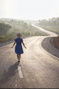 Rear view of woman walking on road against sky