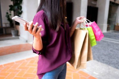 Midsection of woman holding mobile phone on street