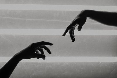Cropped image of hands reaching towards each other against wall