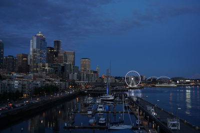 Illuminated buildings by river against sky at night