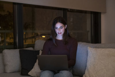 Young woman using phone while sitting on sofa at home