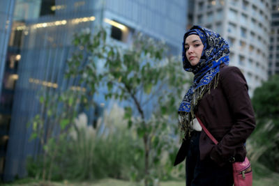 Young woman looking away while standing against plants