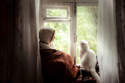 Toddler girl with a cat sitting on the window, concept of a fabulous childhood and favorite animals