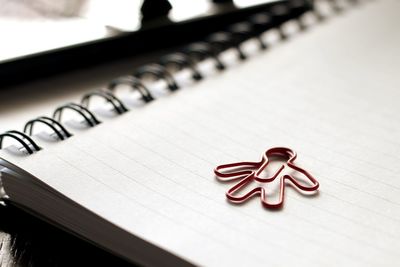 Close-up of human shaped paper clip on spiral notebook