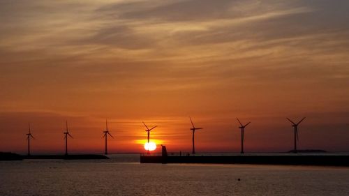 Silhouette wind turbines against orange sunset sky seen from amager strandpark