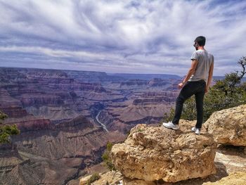 Man standing on rock by mountain against sky