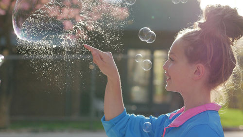 Side view of smiling teenage girl bursting bubble outdoors