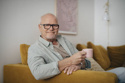 Portrait of senior man with coffee cup sitting on sofa at home