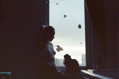 A woman stands in front of a window in an apartment