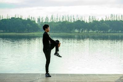 Side view of man standing by lake against sky